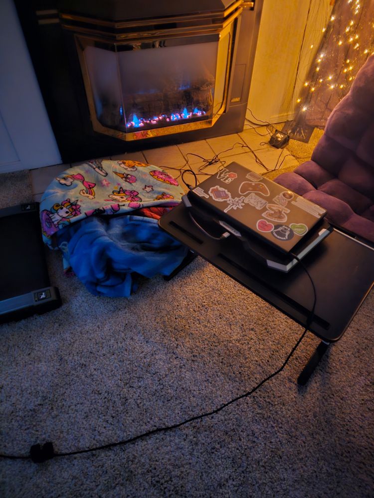 A purple floor chair with a black tray holding a laptop and a round dog bed in front of a fireplace. 
