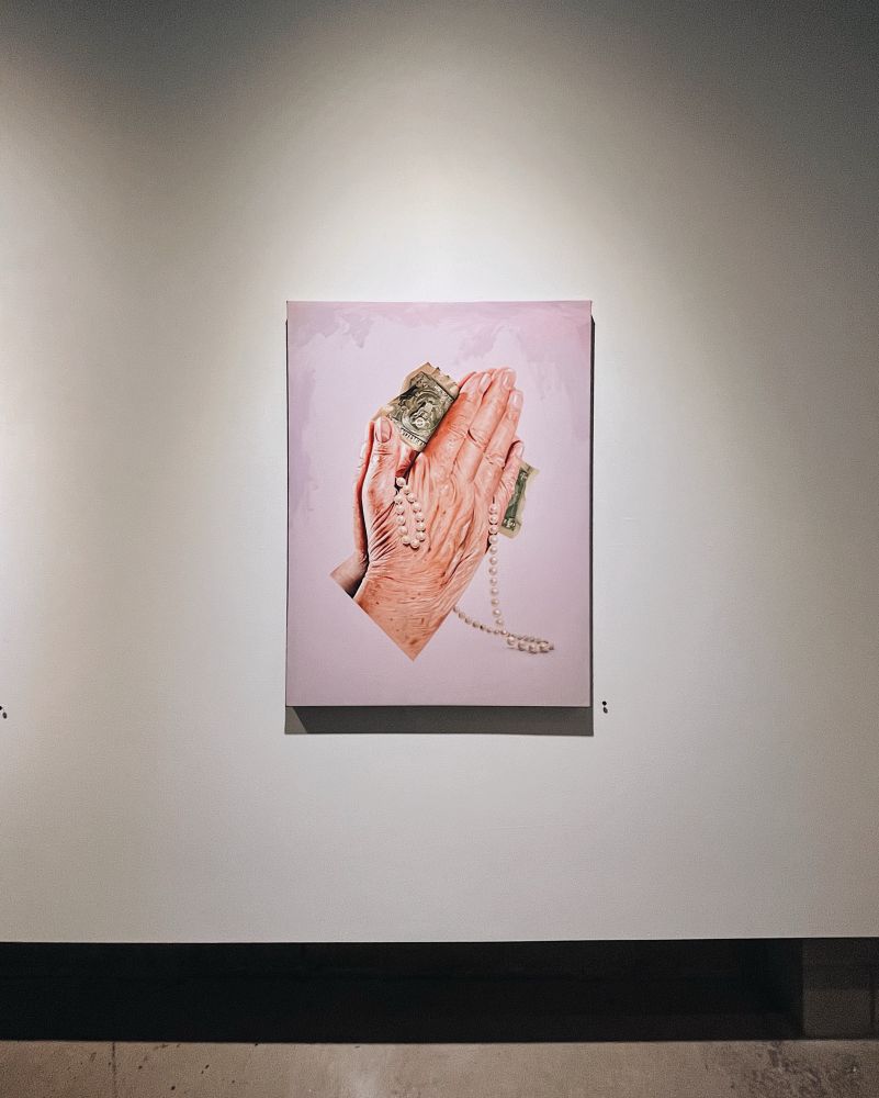 Painting of two praying hands with a dollar bill and a pearl necklace.