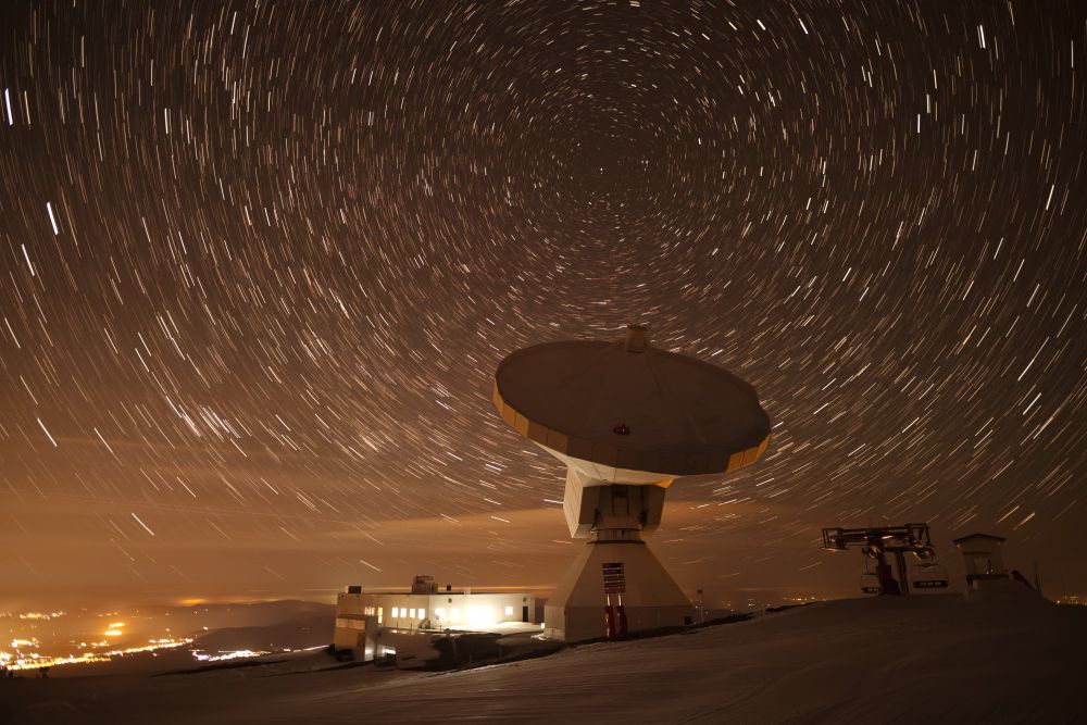 A time-lapsed image of the IRAM-30m telescope in front of a dark orange sky filled with stars