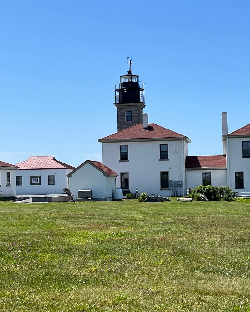 The lighthouse at Beavertail State Park in Jamestown, RI. The lighthouse is behind a large white building with a red roof.