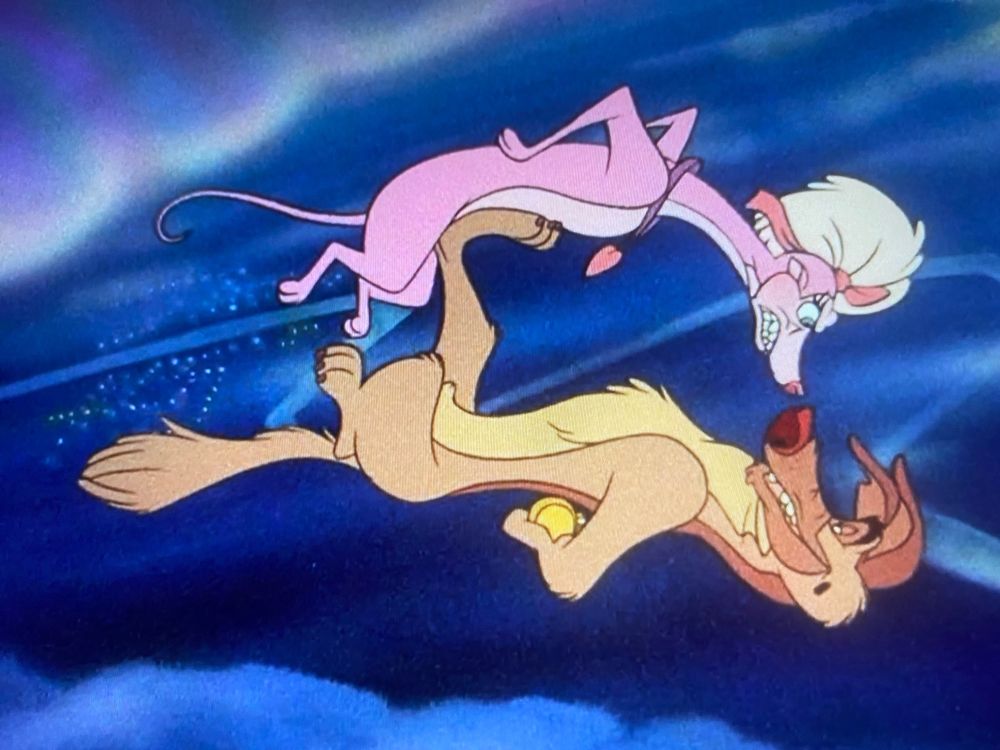 Screenshot from All Dogs Go To Heaven, featuring Charlie (a German shepherd mix) using one back foot to keep Annabelle (pink Whippet angel) from retrieving the watch he’s hiding behind his back as they float through the air & clouds high above a nighttime New Orleans cityscape at distance.