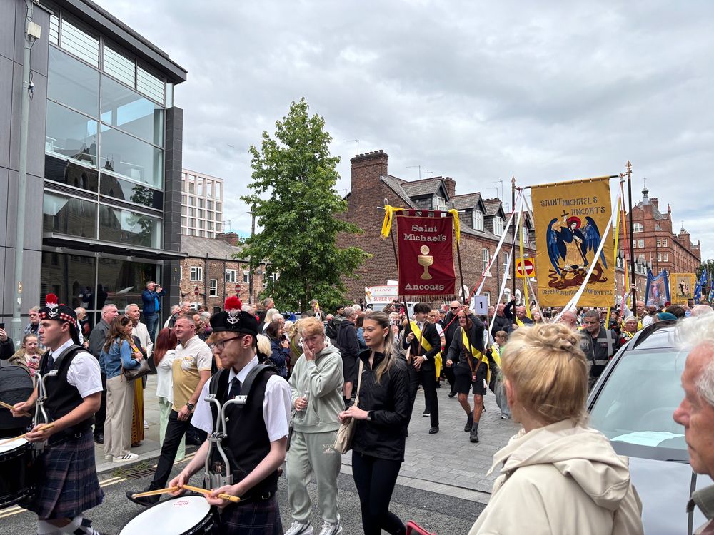Crowds take part in the Madonna del Rosario procession in Ancoats, with banners for Saint Michael’s and a pipe band leading the way along a busy street.