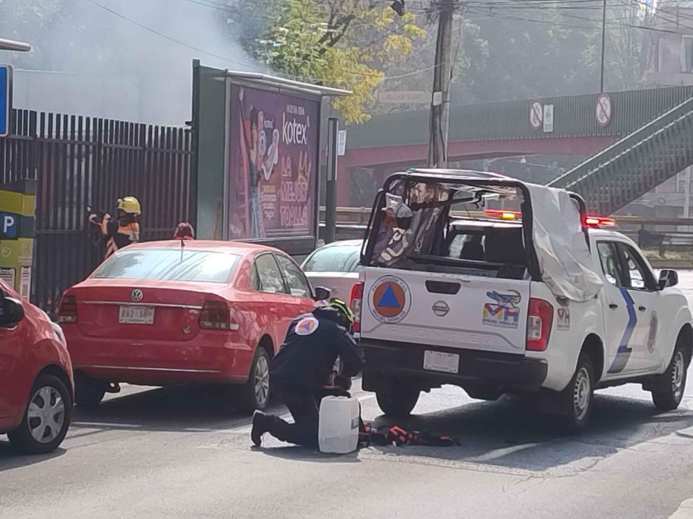  A white pickup truck, labeled as being from the civil defense department of the borough of Miguel Hidalgo, has parked on the street in front of the fire. A worker is filling a backpack-and-sprayer assembly from a 5 gallon jug. Not sure they're fully equipped for this.