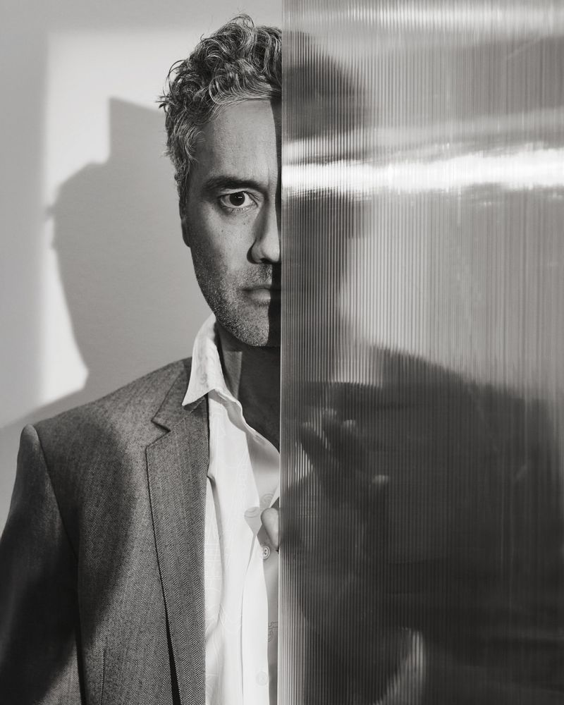 A black and white photo of Taika Waititi, partly obscured by glass