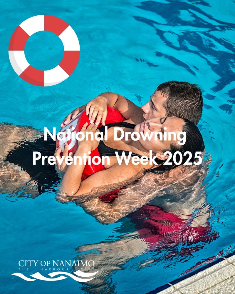 A person in a swimming pool holds another individual wearing a red and white life preserver. Text reads 'National Drowning Prevention Week 2025.' A logo in the bottom left corner says 'City of Nanaimo THE HARBOUR' with wave graphics.
