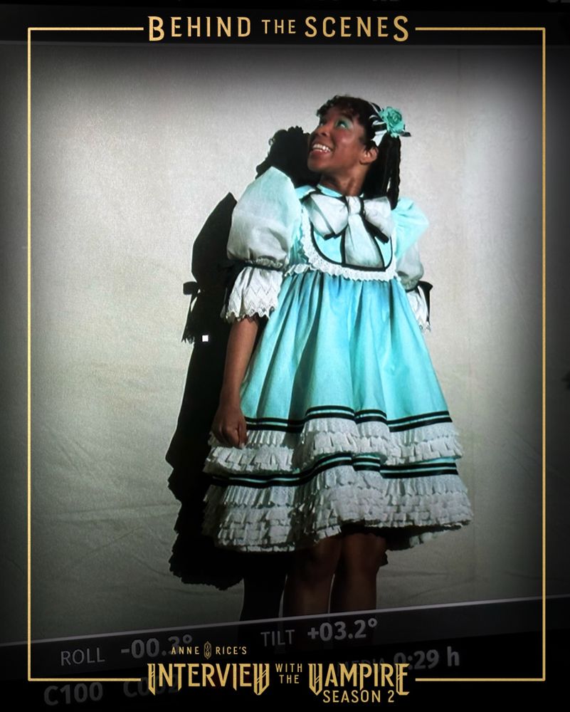 Delainey Hayles in Claudia’s stage costume filming a scene from E4. A white screen is behind her. She’s looking up and singing.
