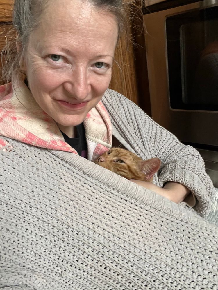 woman in large sweater with cuddly cat peering out 