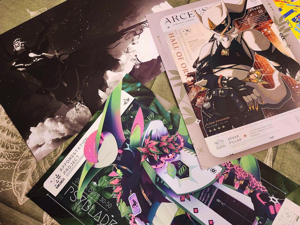 image is a photograph of an assortment of art prints featuring anthropomorphic pokemon and otherworldly animals.