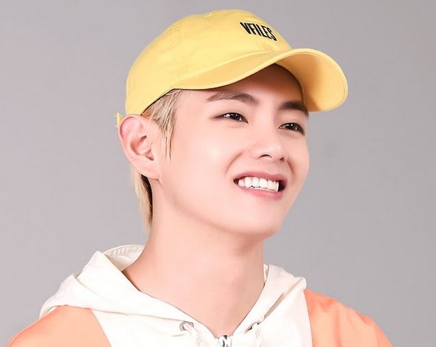 From BTS World.  Blond Tae smiling with a yellow cap and blond hair - cream and peach colored jacket.  Perfect skin. Stellar eyebrows. Handsome as ever, yo. 