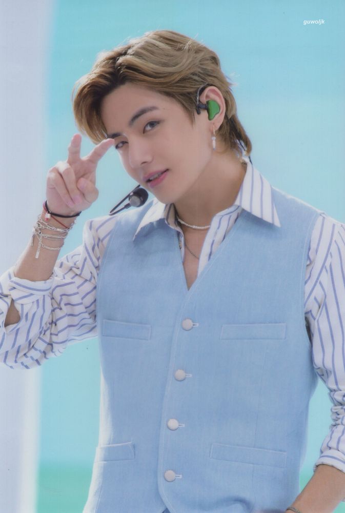 Light brown hair, V to face, light blue vest over white and blue stripe shirt, green in-ear, mic, looking at you.  Yes he is. So handsome. 