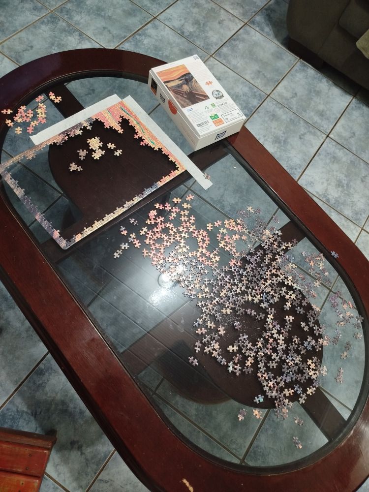 foto um pouco mais de longe mostrando a mesa inteira, na parte esquerda da mesa é onde o quebra cabeça está sendo montado, e no meio e na parte direita estão as peças 