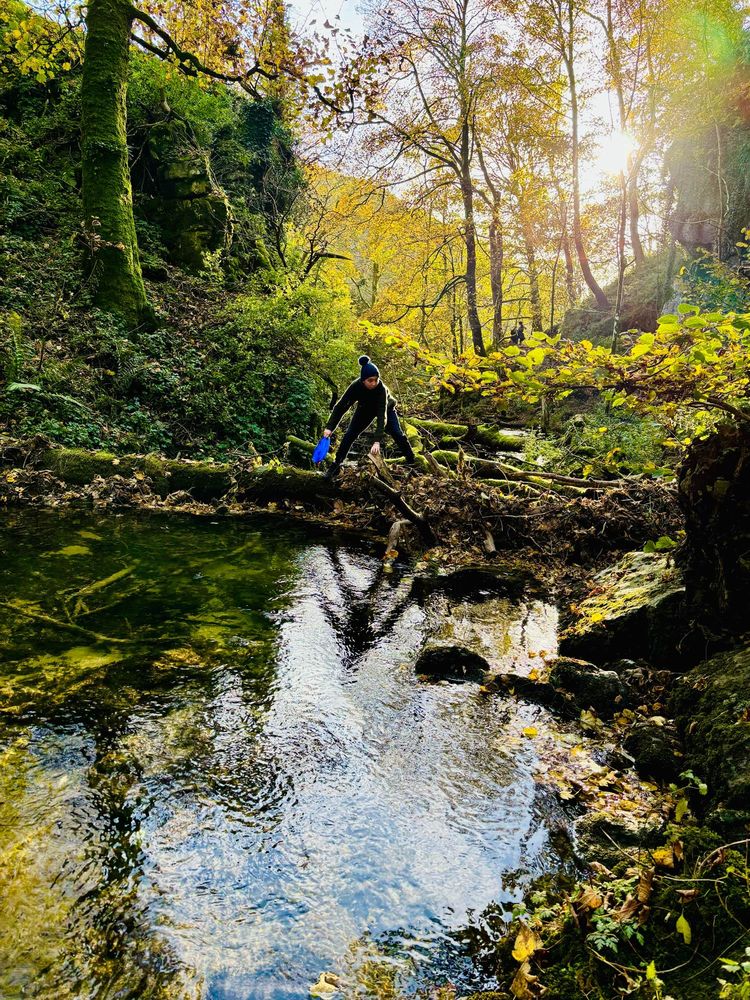 Boy removing plastic trash from Janet’s Foss in Malham. Lots of green trees and watery reflections. 