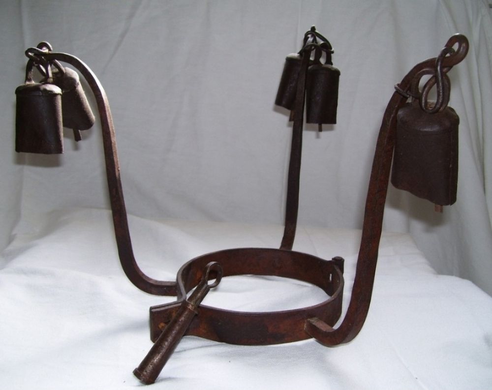 A chattel enslavement, heavy, forged metal, torture collar that was locked around enslaved peoples' necks who had tried to escape. It has 3 arms that stretch out & upward around the head, with bells on the ends.