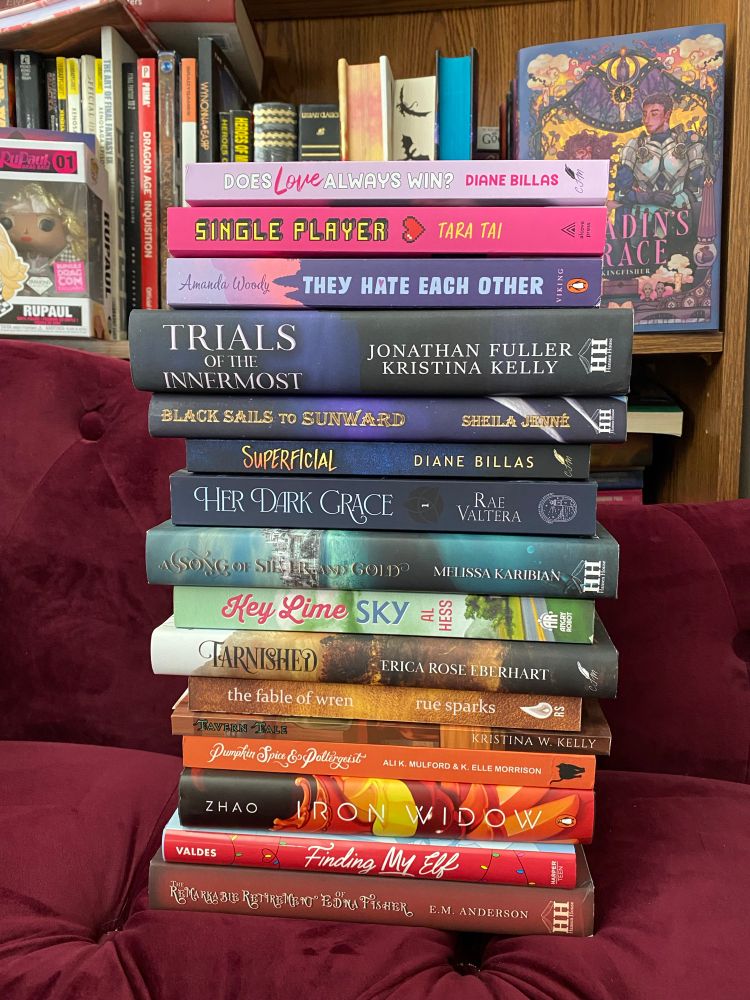 A stack of books organized by ROYGBIV on a maroon chair. Books from top to bottom: DOES LOVE ALWAYS WIN?
SINGLE PLAYER
THE HATE EACH OTHER
TRIALS OF THE INNERMOST
BLACK SAILS TO SUNWARD
SUPERFICIAL
HER DARK GRACE
AS SONG OF Silver and Gold
Key Lime SKY
TARNISHED
the fable of wren
TAVERN TALE
Pumpkin Spic & Poltergeist
IRON WIDOW
VALDES
Finding My ELf
The Remarkable Retirement of Edna Fisher