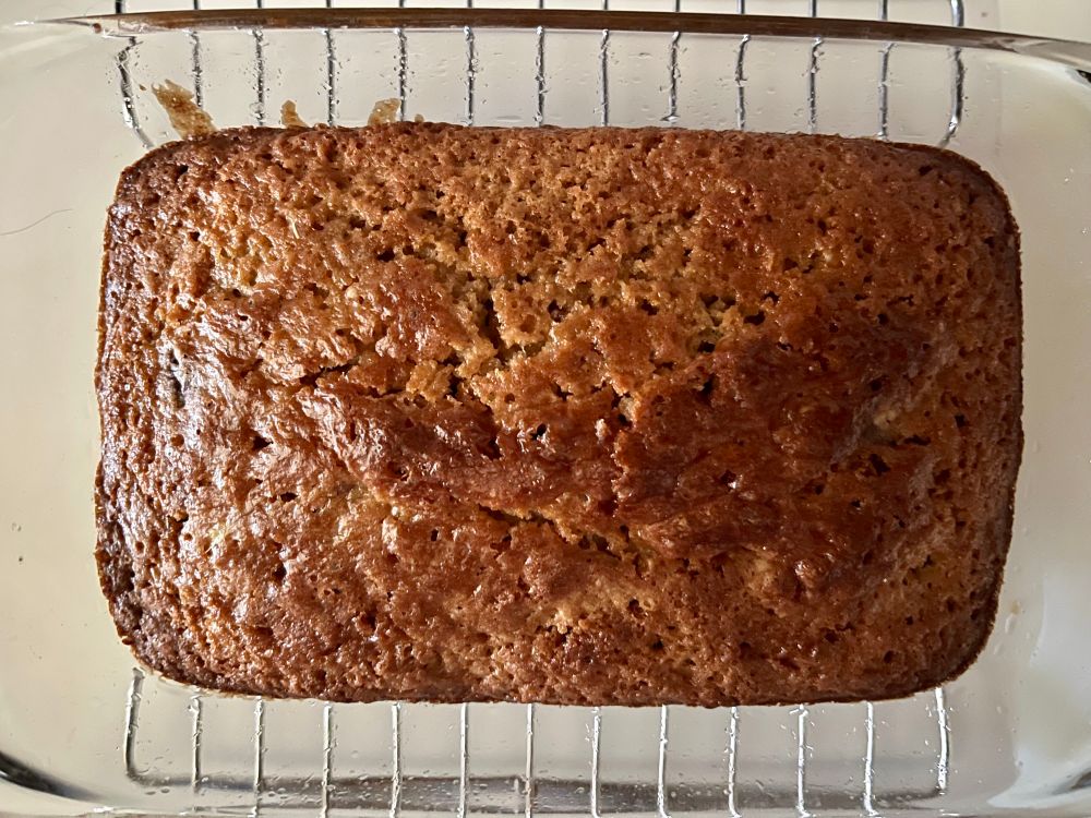 Top down photo of golden brown loaf in glass pan on top of steel rack. 