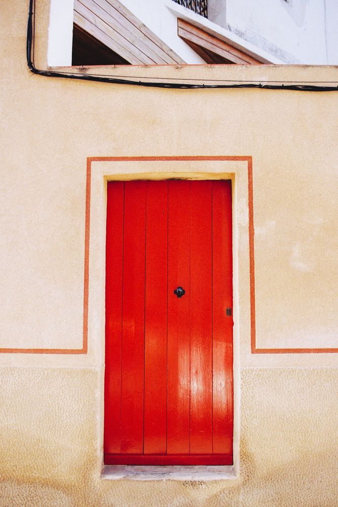 Photograph of a red door with a red line running along the edge of the door and extending horizontally to the sides. Above you can see cables and a low wall.