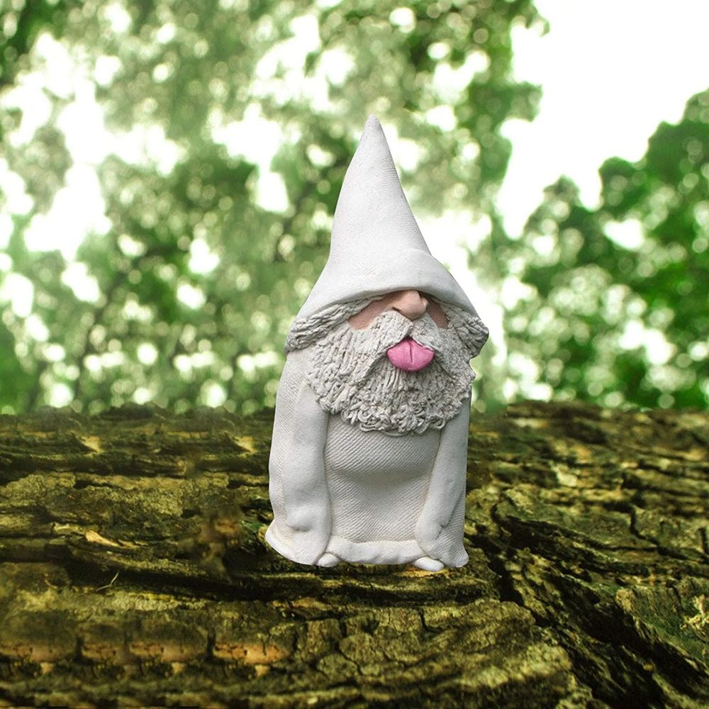 Une statuette de gnome à chapeau pointu posée sur une branche d'arbre, et tirant la langue