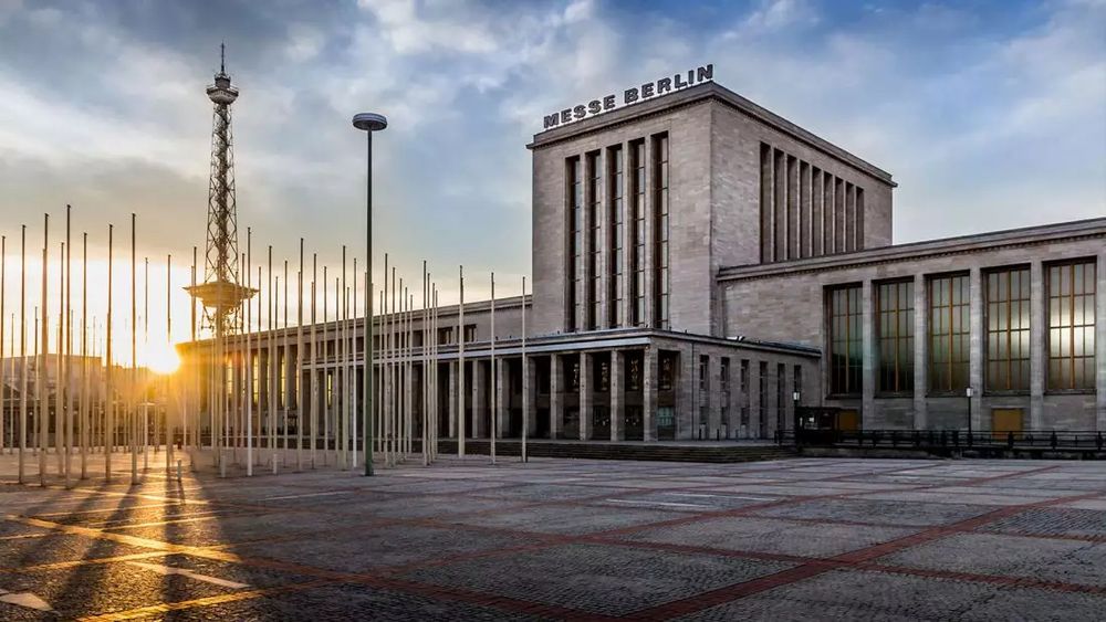 Vue en contrejour à l'aube des bâtiments cubiques épurés et kolossaux du Messe (Palais des congrès) de Berlin, sur sa place dégagée, avec la tour radio à côté en ombre chinoise près du jardin japonais. © Messe Berlin