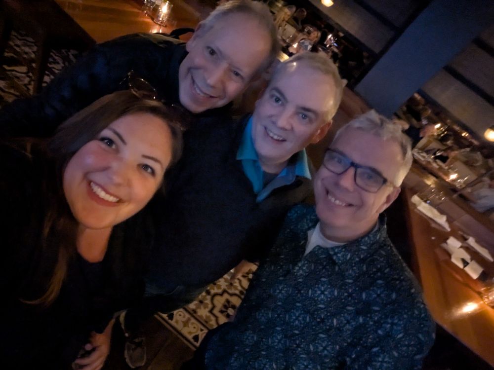 Three men and a woman in a selfie at a restaurant 