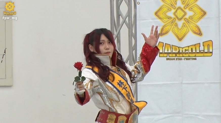 Utami Hayashishita holds up a red rose as she walks into the building in her red and white robe. Her hair parted in the middle, about chin length to the sides of her face and twice as long behind the ears in two high pigtails.