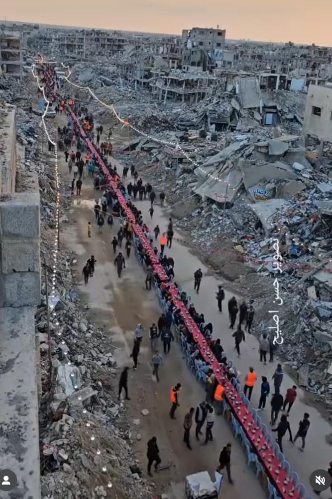 Pic of a narrow path carved through the rubble of Khan Yunis, filled with tables and party lights to celebrate the an Iftar meal for Ramadan