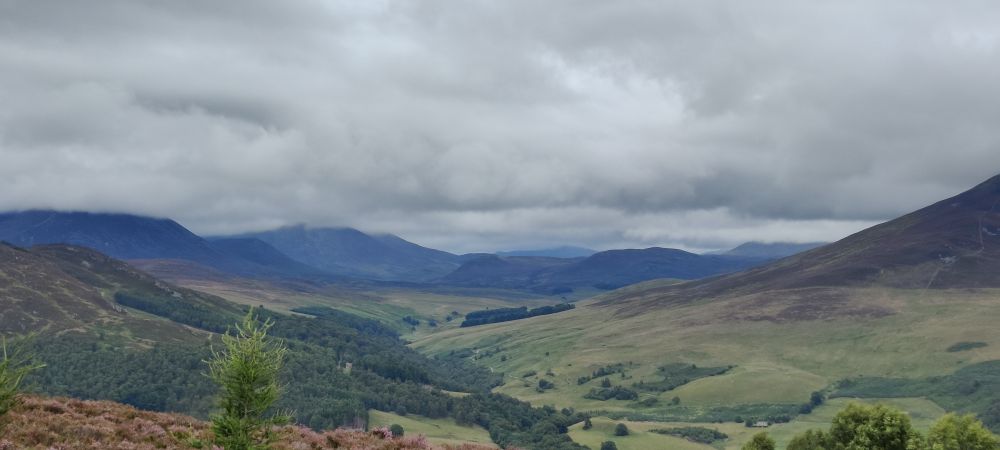 Photo of an overcast valley in Scotland with some cloud capped mountains in the distance.