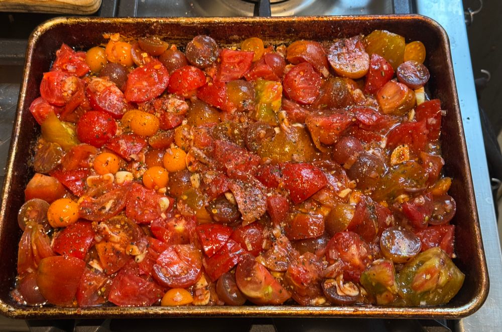 A sheet pan filled with raw tomatoes and dressing 