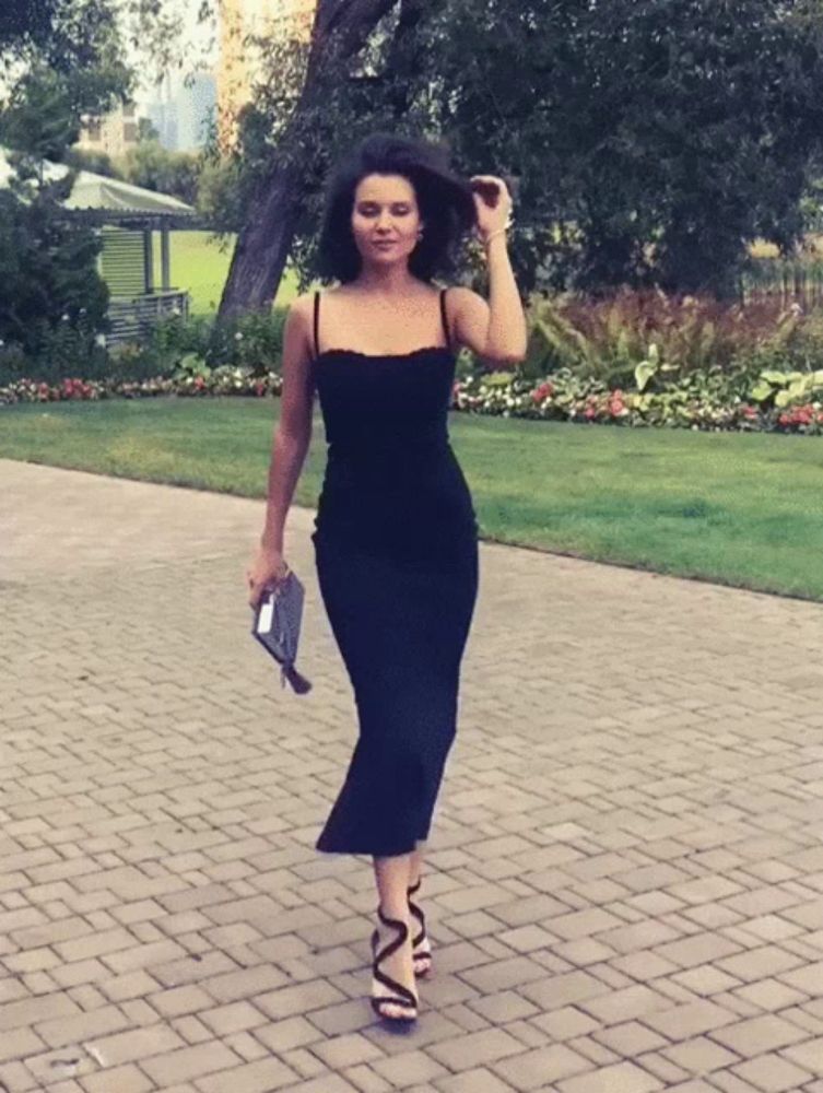 a woman in a black dress and heels is walking down a brick driveway