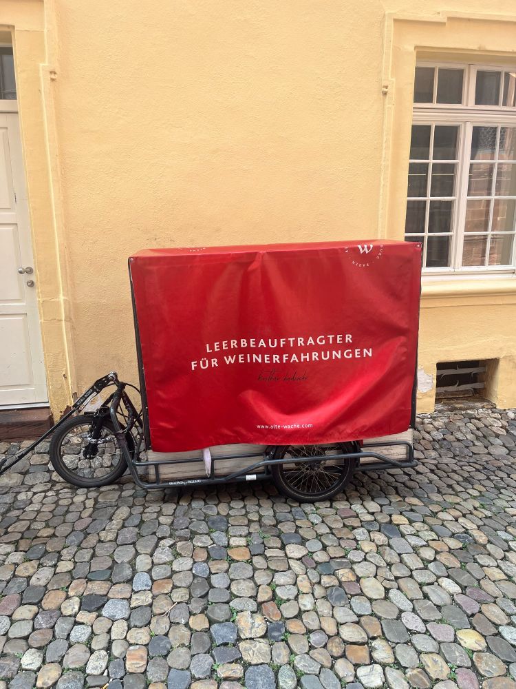 Auf dem Foto sieht man einen Anhänger einer Weinhandlung mit der Aufschrift: „Leerbeauftragter für Weinerfahrungen“