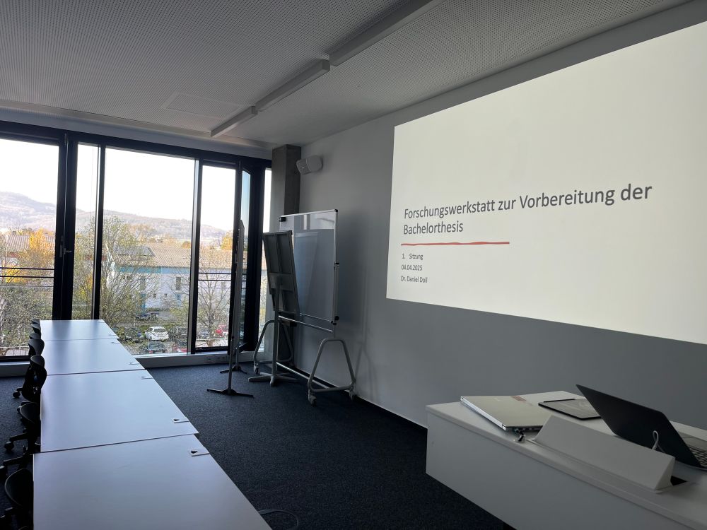 Foto von blühenden Bäumen vor dem Raum der Hochschule. Im Vordergrund die erste Folie der Präsentation.