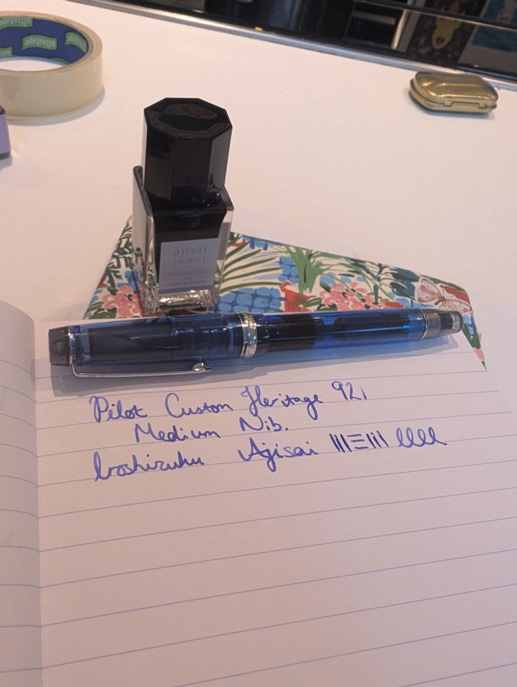 Blue, transparent fountain pen resting on a notebook with blue ink in a bottle. 