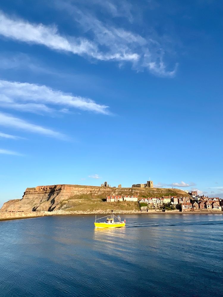 Yellow boat on a blue sea, Whitby abbey in the cliff in the background