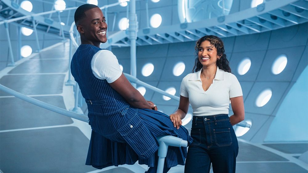 Le 15e Docteur et Belinda Chandra dans le TARDIS, grand espace bleuté avec des ronds lumineux sur les murs et une pente jusqu'à l'étage supérieur 