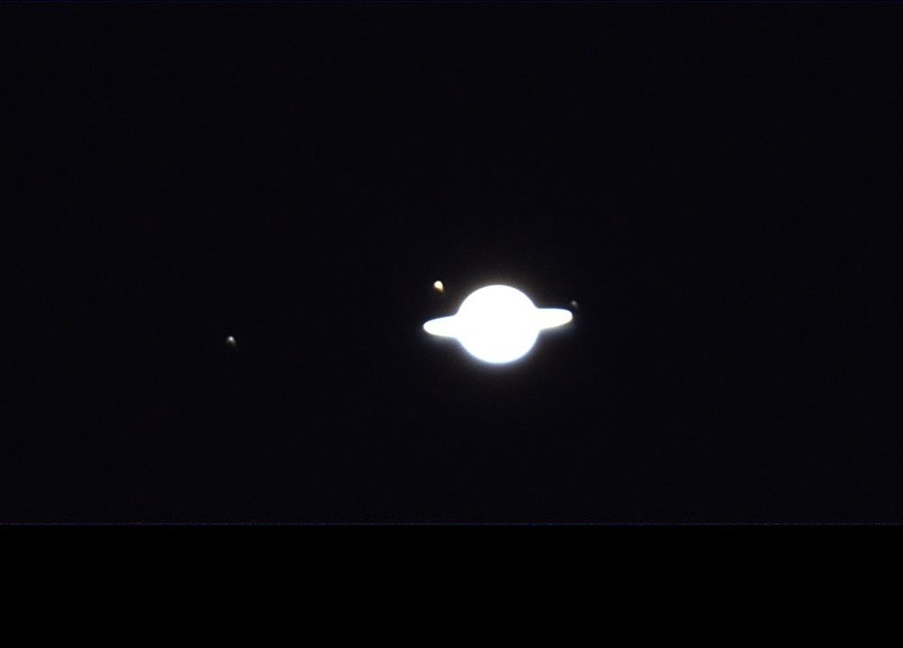 Saturn’s moons Rhea (far left), Titan (left above the rings), Dione (right just above the rings).