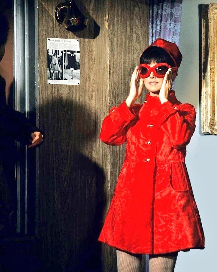 Marlo Thomas is wearing a red pillbox hat, a red faux fur coat and matching red faux fur covered Oliver Goldsmith Yuhu style sunglasses.