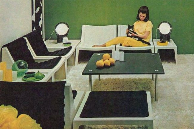Woman holding a black and white cat in a room filled with space age black and white furniture. The walls are green and white, and there are pops of yellow, including the woman's outfit. Ikea catalog 1970 