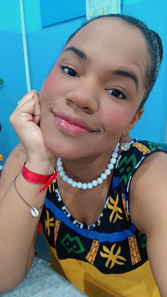 Foto minha de cabelo preso com coque com queixo apoiado na mão de vestido mostarda com estampado étnico