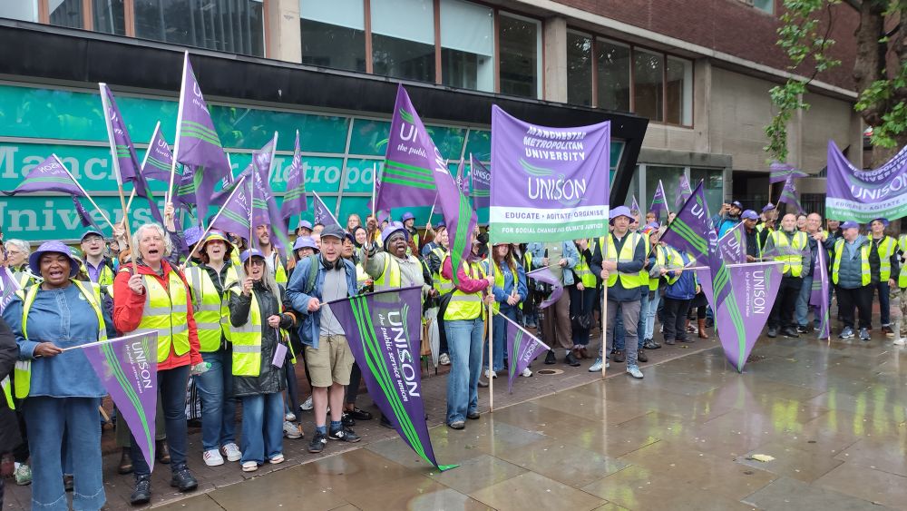 Picture of ~100 UNISON members in hi-vis vests, waving purple flags. We’re picketing in the rain, but everyone is cheering and chanting - the mood is clearly high. 💪