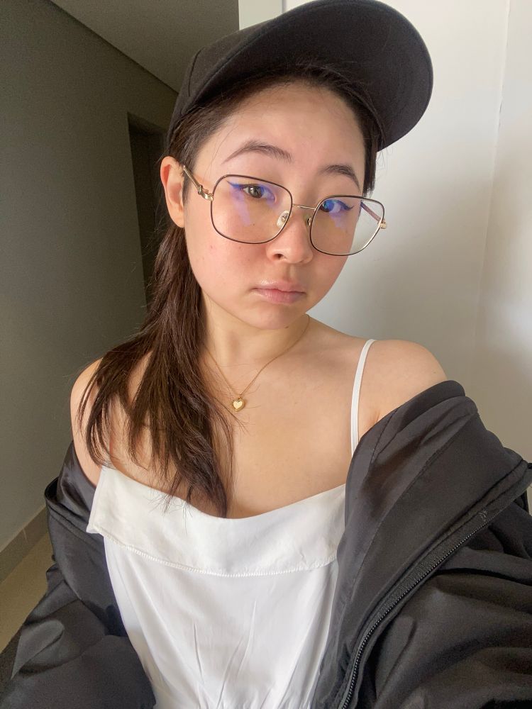 Selfie minha. Sou mulher amarela de cabelos longos, lisos de cor castanho clara. Estou olhando pra câmera. Uso um vestido branco e blusa (só é visível até altura do estômago) e um boné preto. Meu cabelo está preso e é possível ver a ponta cobrindo meu ombro esquerdo