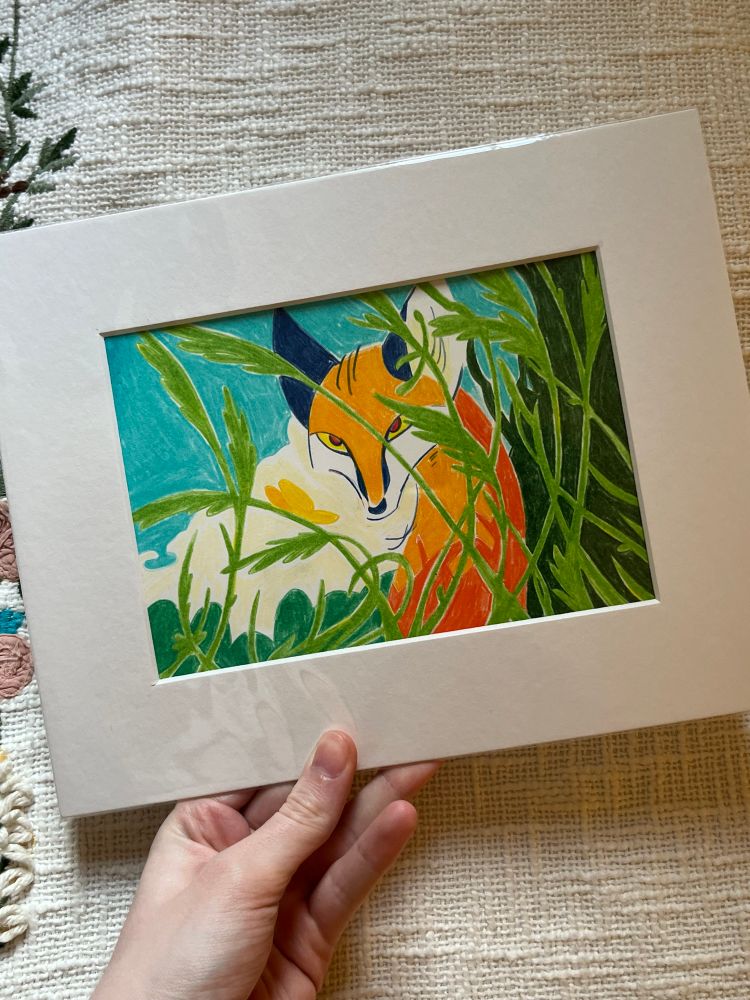 A photo of a matted coloured pencil illustration of a fox behind the cover of long grass