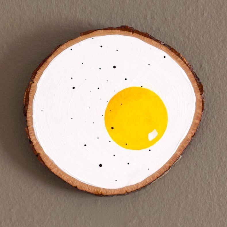 photo of a painting of a fried egg on a piece of wood with bark