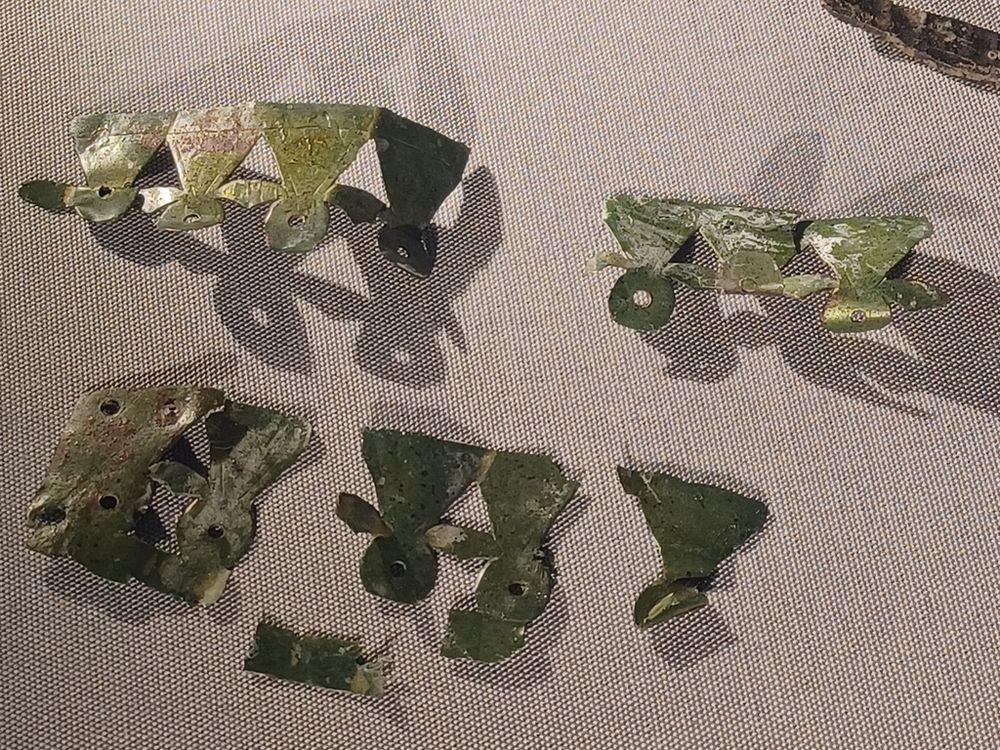 A photograph showing several fragments of decorative copper-alloy sheet in a museum case. The sheet is pierced, and has been made into an openwork design of wedges and circles.