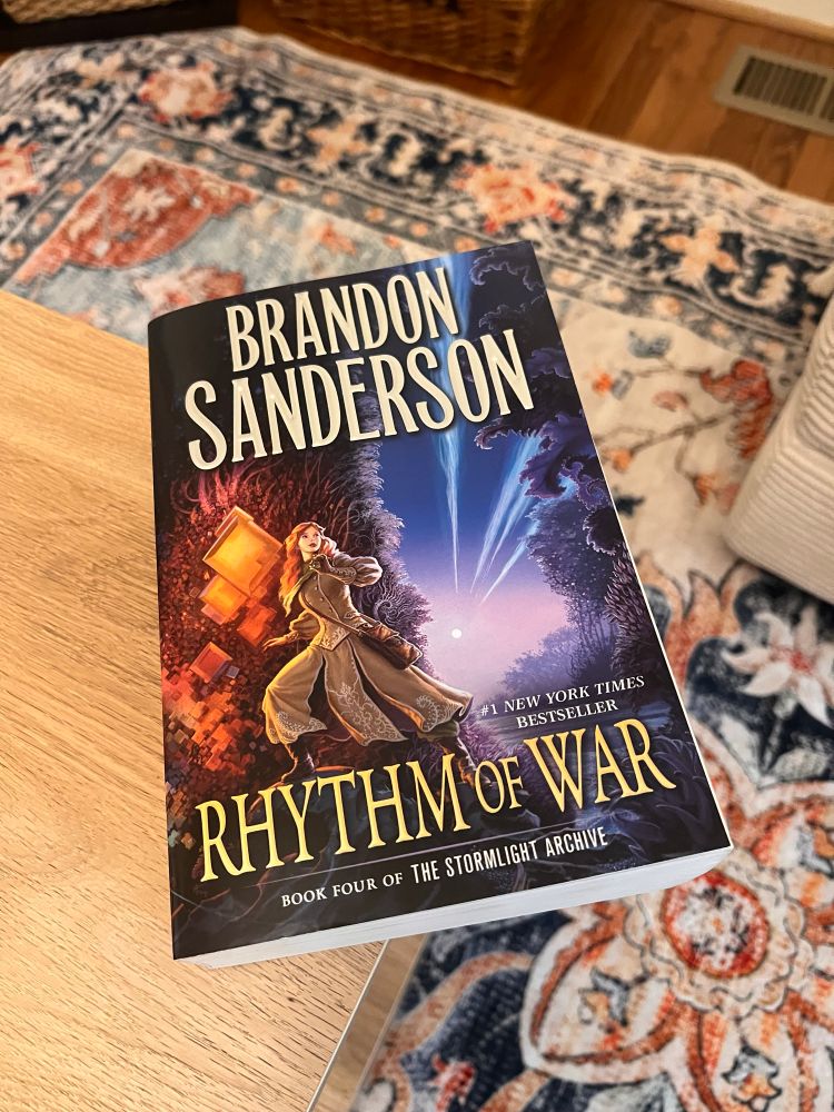 A photo of Brandon Sanderson’s book Rhythm of War sitting on the edge of a coffee table.