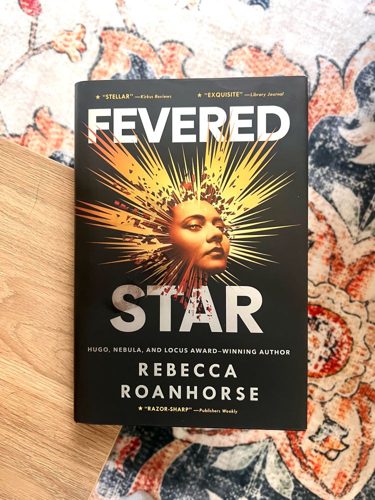 The book, Fevered Star, on the edge of a coffee table. A patterned carpet is in the background.