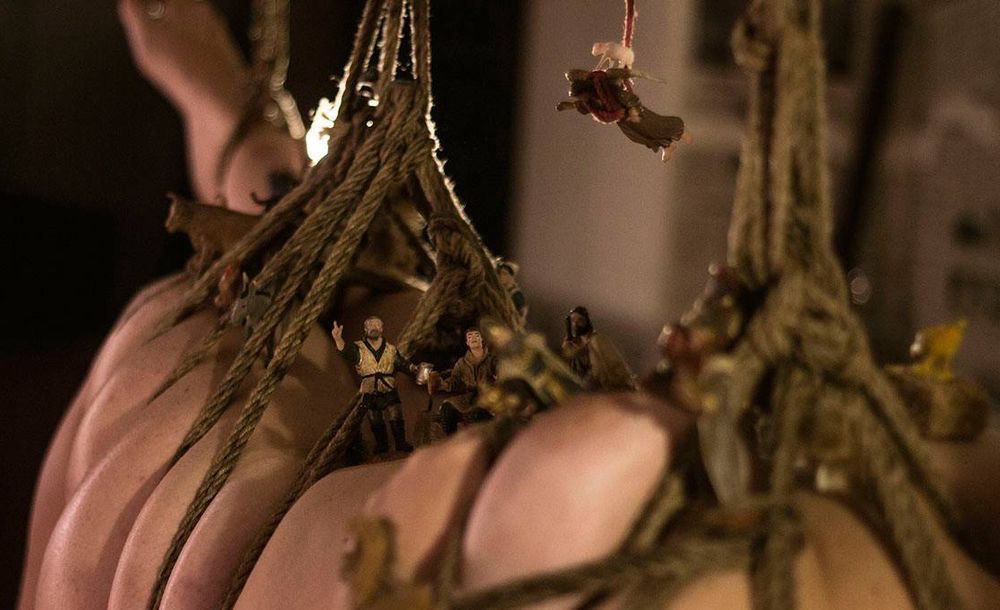 a woman tied and suspended, wearing a whole nativity scene. black background.