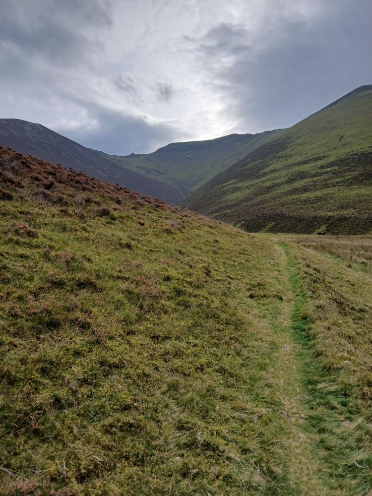 The grassy path up Hope Gill, near Lorton Vale, Cumbria, with Hopegill Head at the top, and low grey skies above the hills.