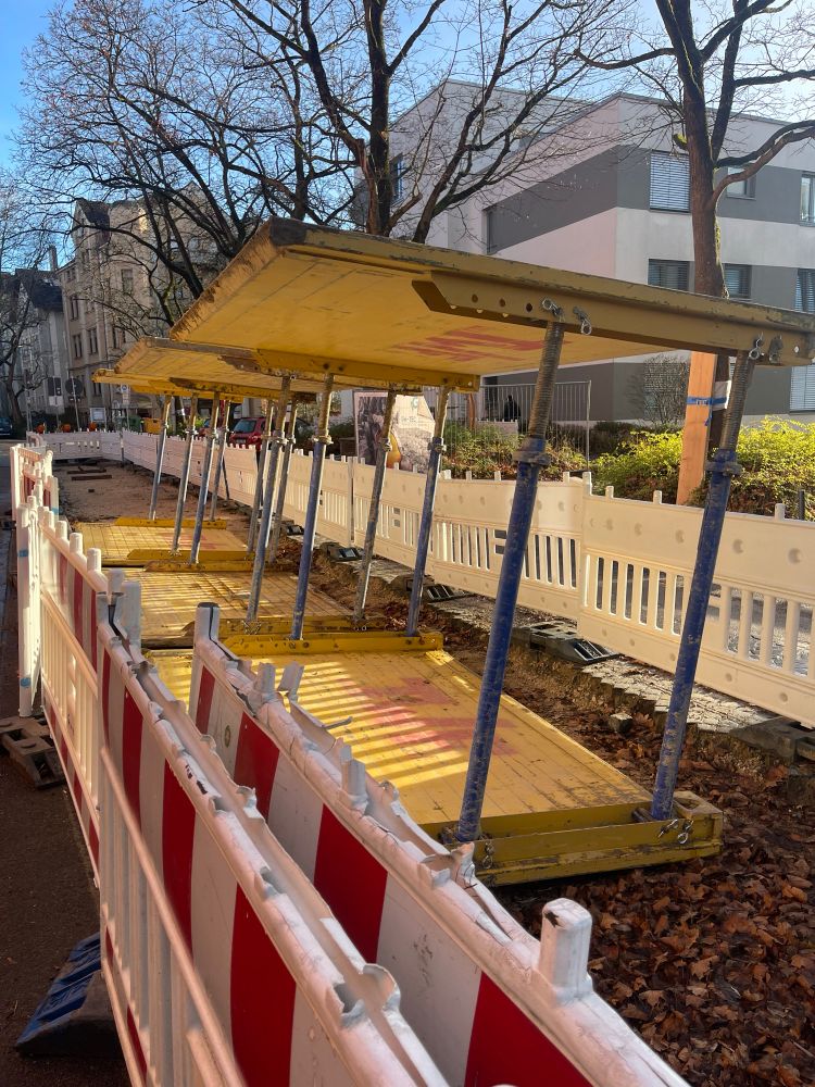 ein bauabschnitt neben einer straße im wohngebiet auf dem quer trennwände liegen sodass sie beinahe aussehen wie eine überdachte  outdoor bar