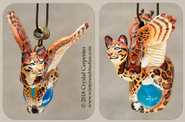 A winged cat pendant, painted with wildcat like spots, sits on a blue orb.