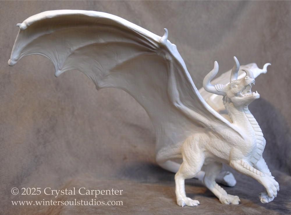 A dragon sculpture, in a pose with two feet on the ground and ready to charge. His mouth is open, as if letting out a roar. His wings are spread out, as he displays his bull and rhino like horns. He is currently pure white, and in need of colors that match his mighty personality! If he inspires you, you might be the right one to help finish his creation here: https://ko-fi.com/c/974cac76ca