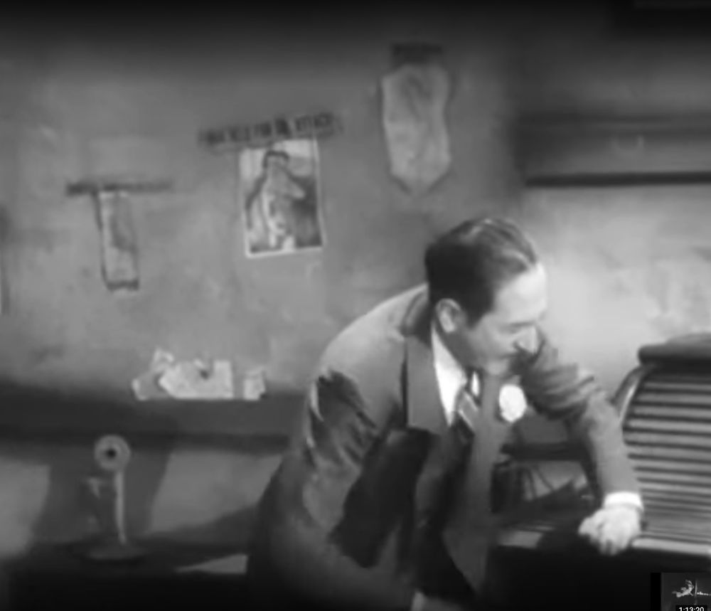 Adolphe Menjou letting some air into the roll-top desk where the fugitive is hiding out, more naked pin-up ladies on the wall behind him.